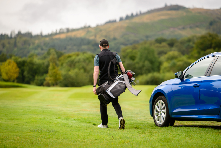 Person with a golf bag on a golf course next to a car